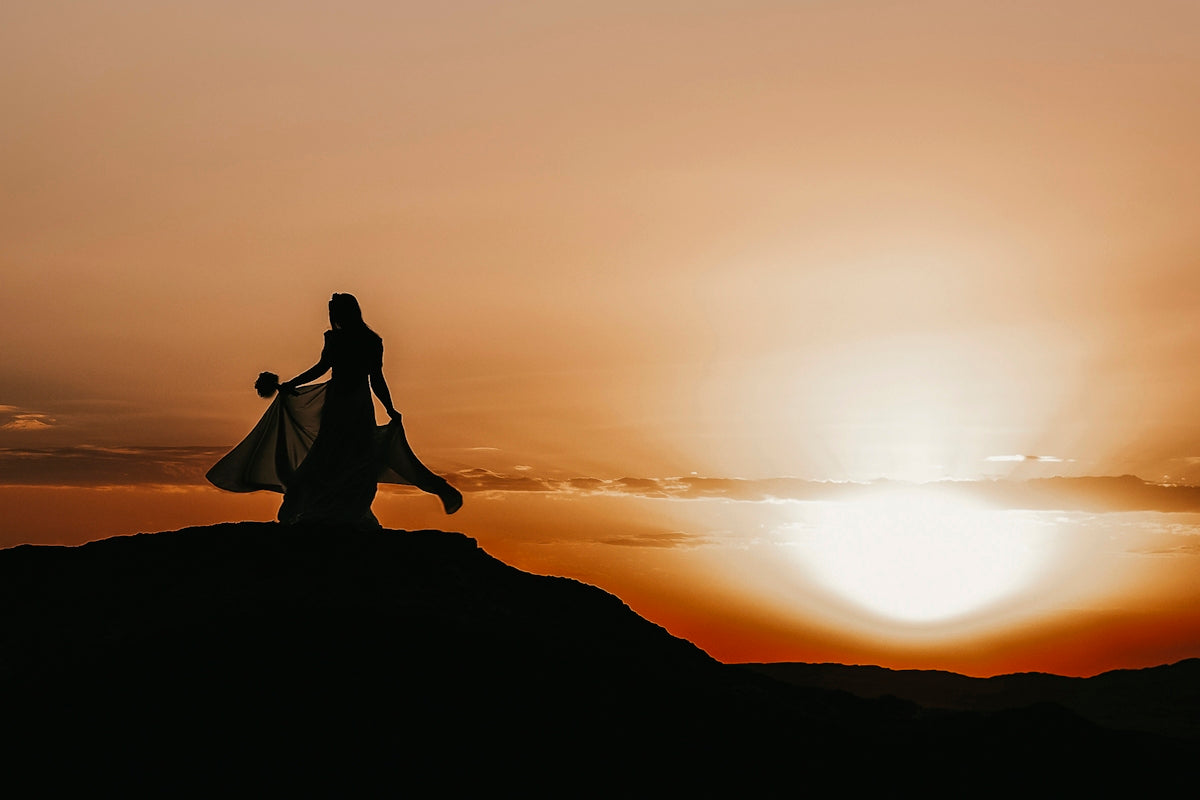 a woman standing on top of a mountain at sunset