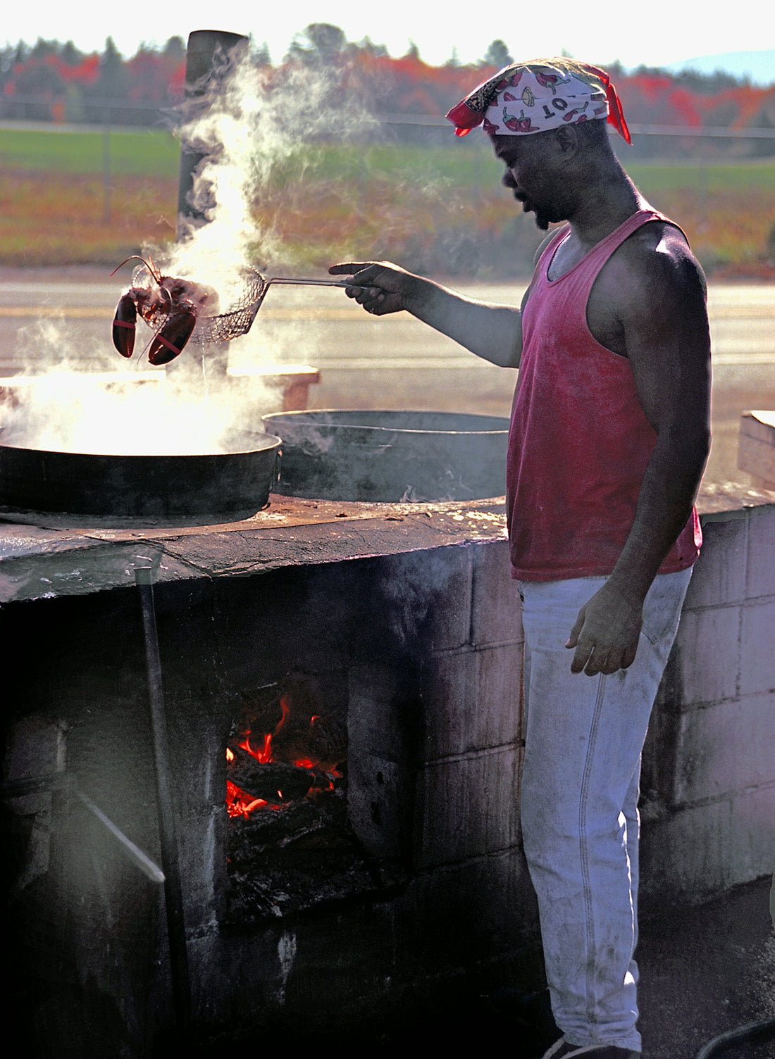 Chef cooks lobster outdoors near a fiery oven.