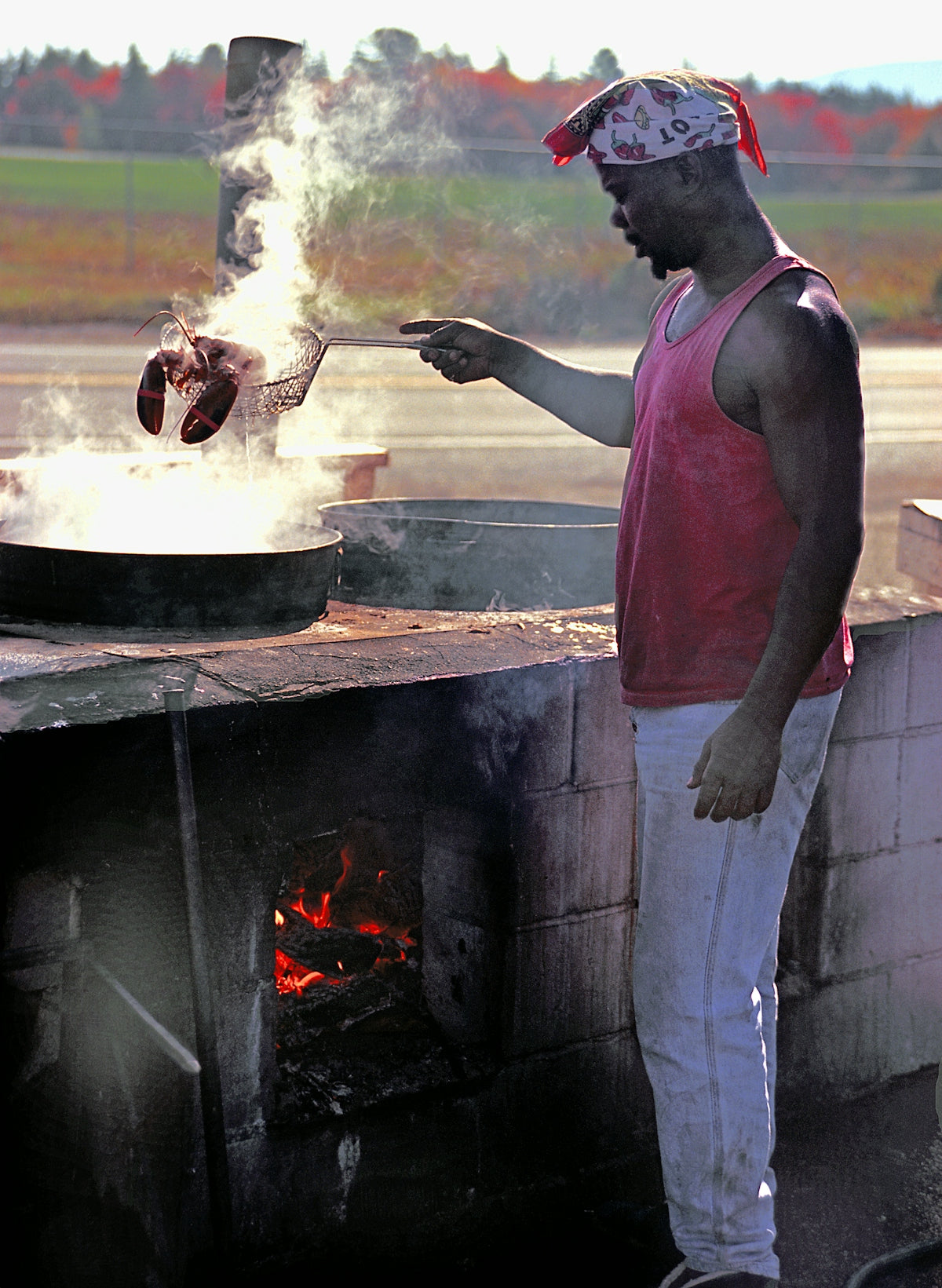 Chef cooks lobster outdoors near a fiery oven.