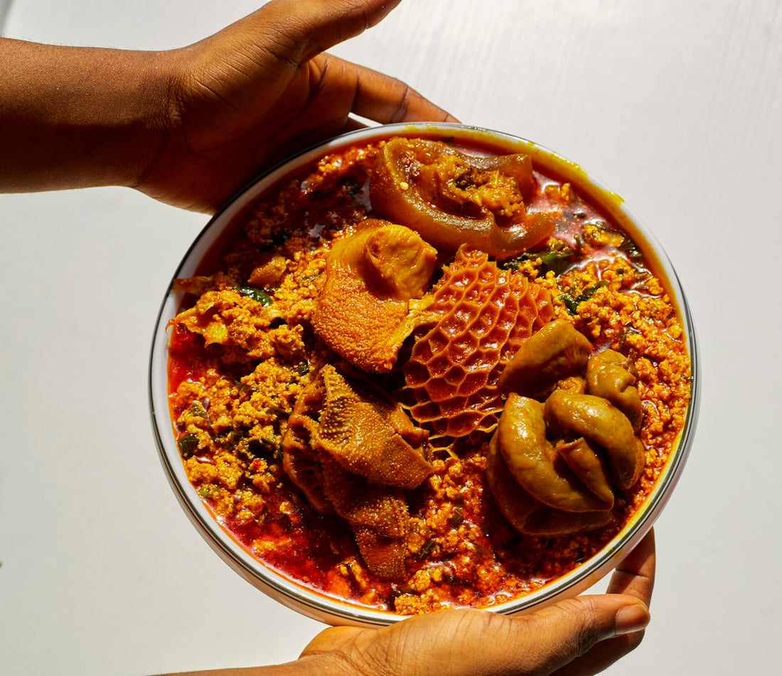 Hands holding a bowl of egusi soup with assorted meats.